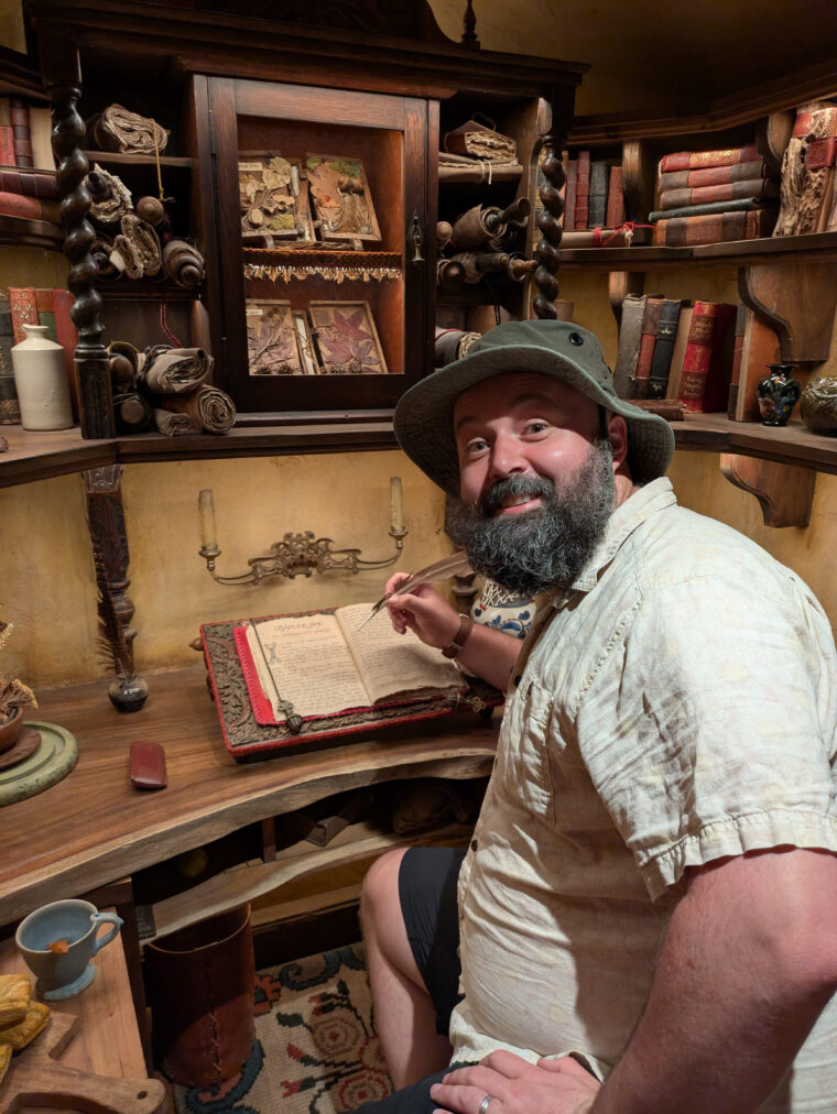 An interview with A World of Milk and R H Wesley An image of Rob Wesley, the author of A World of Milk and Promises. He's looking back over his shoulder while hunched over an olde timey book with an olde timey quill in an olde timey writing salon.